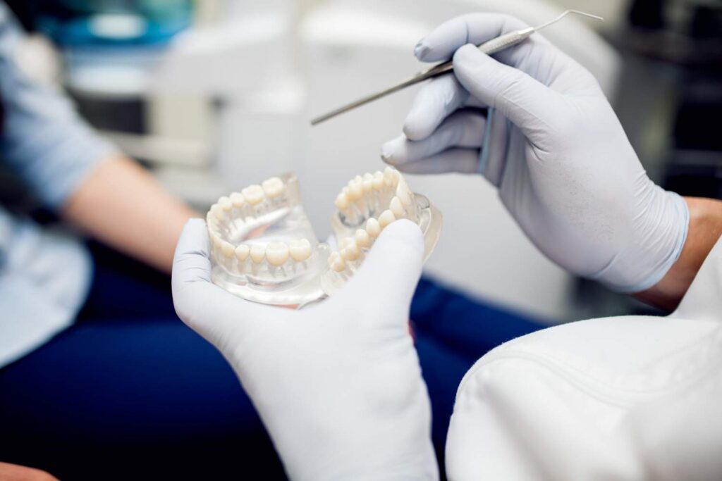 Dentista con guantes sujetando un modelo de prótesis dental